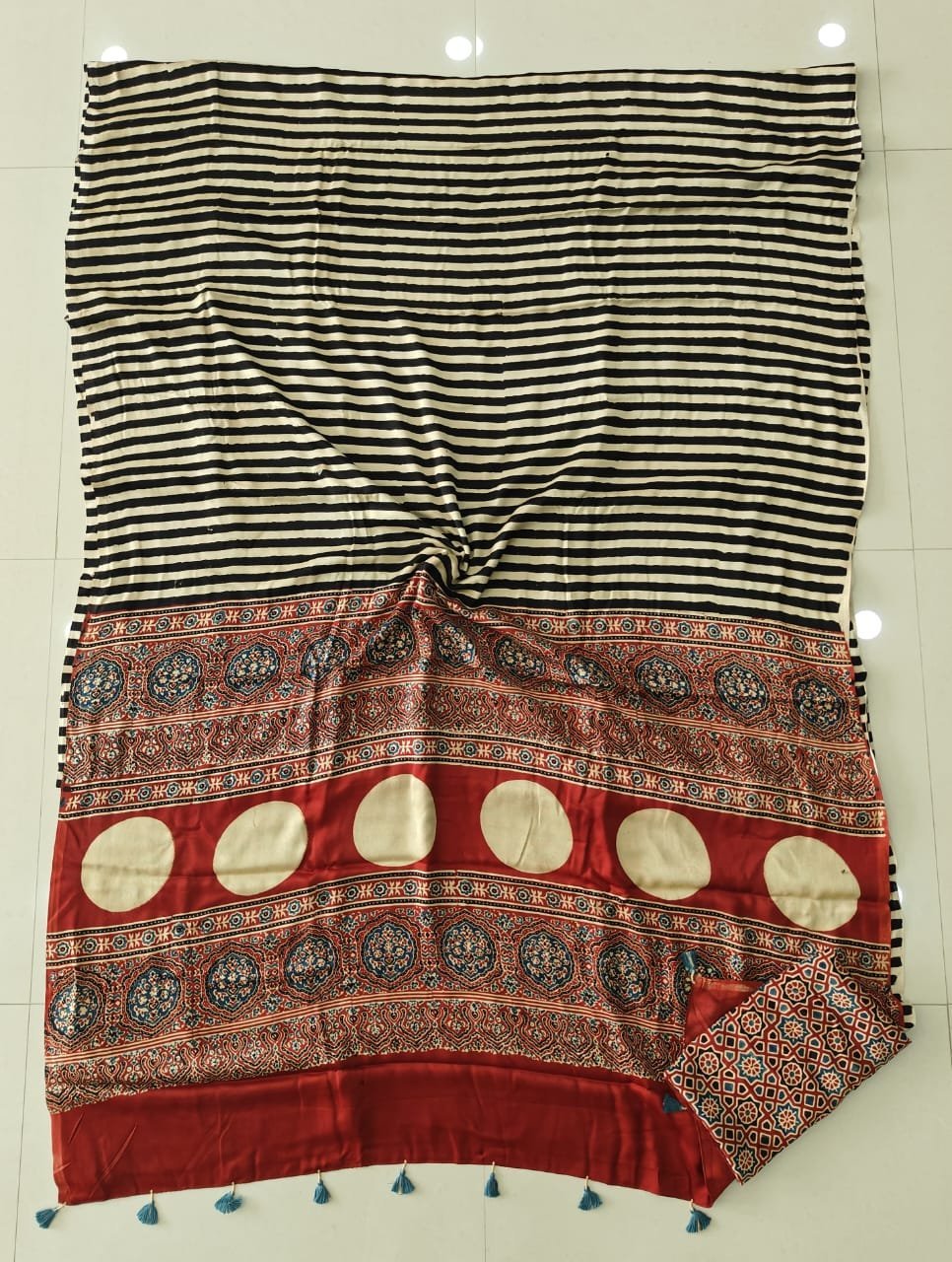 Black and cream striped Ajrakh print modal silk saree with rust red medallion border laid flat