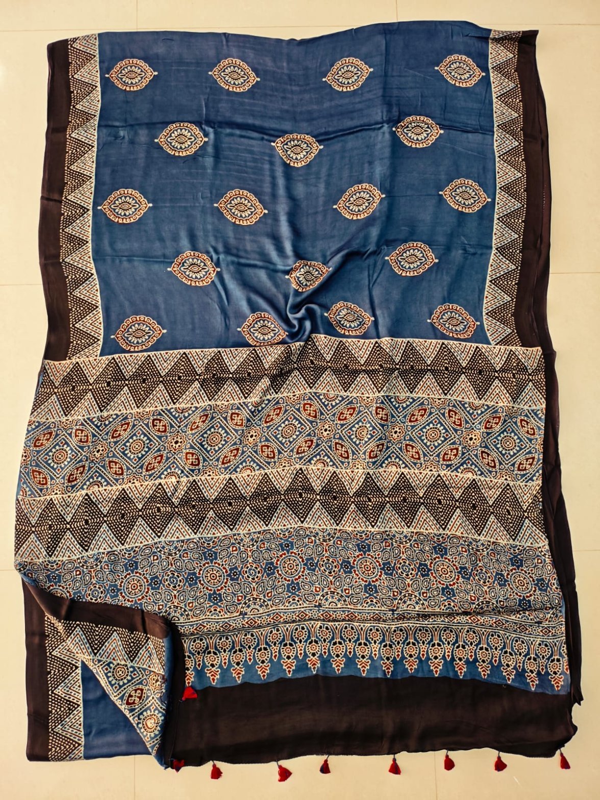 Denim blue Ajrakh print silk saree with paisley booti and chevron pallu, black border with red tassels