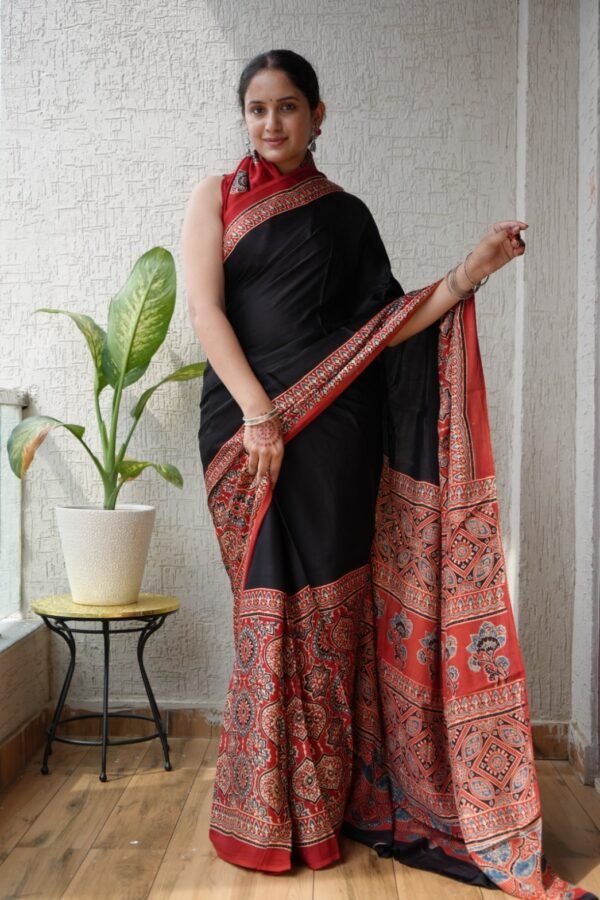 Woman wearing black Ajrakh print modal silk saree with rust-red geometric floral border and pallu