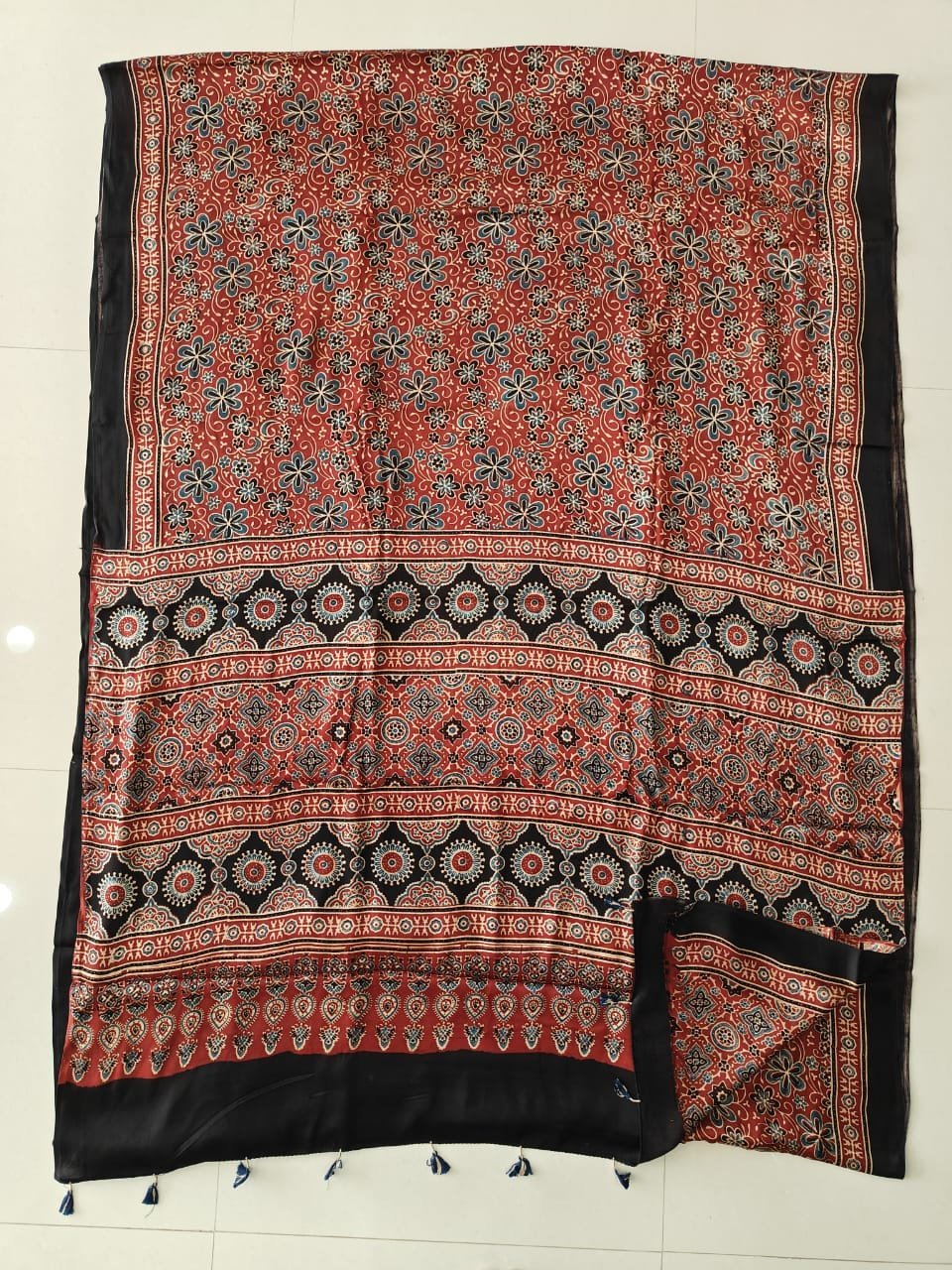 Rust red Ajrakh print pure Modal silk saree with black medallion border and navy tassels